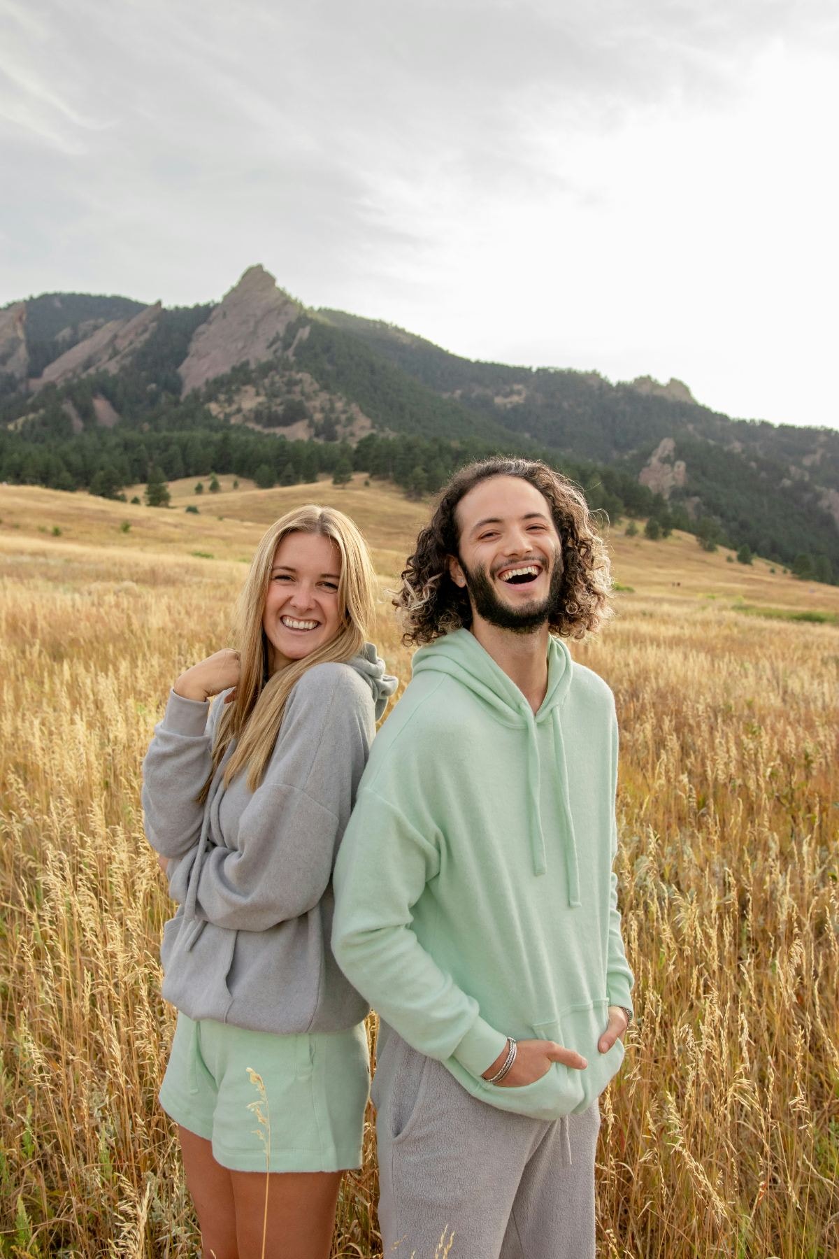 Young couple laughing in a golden field with mountains behind