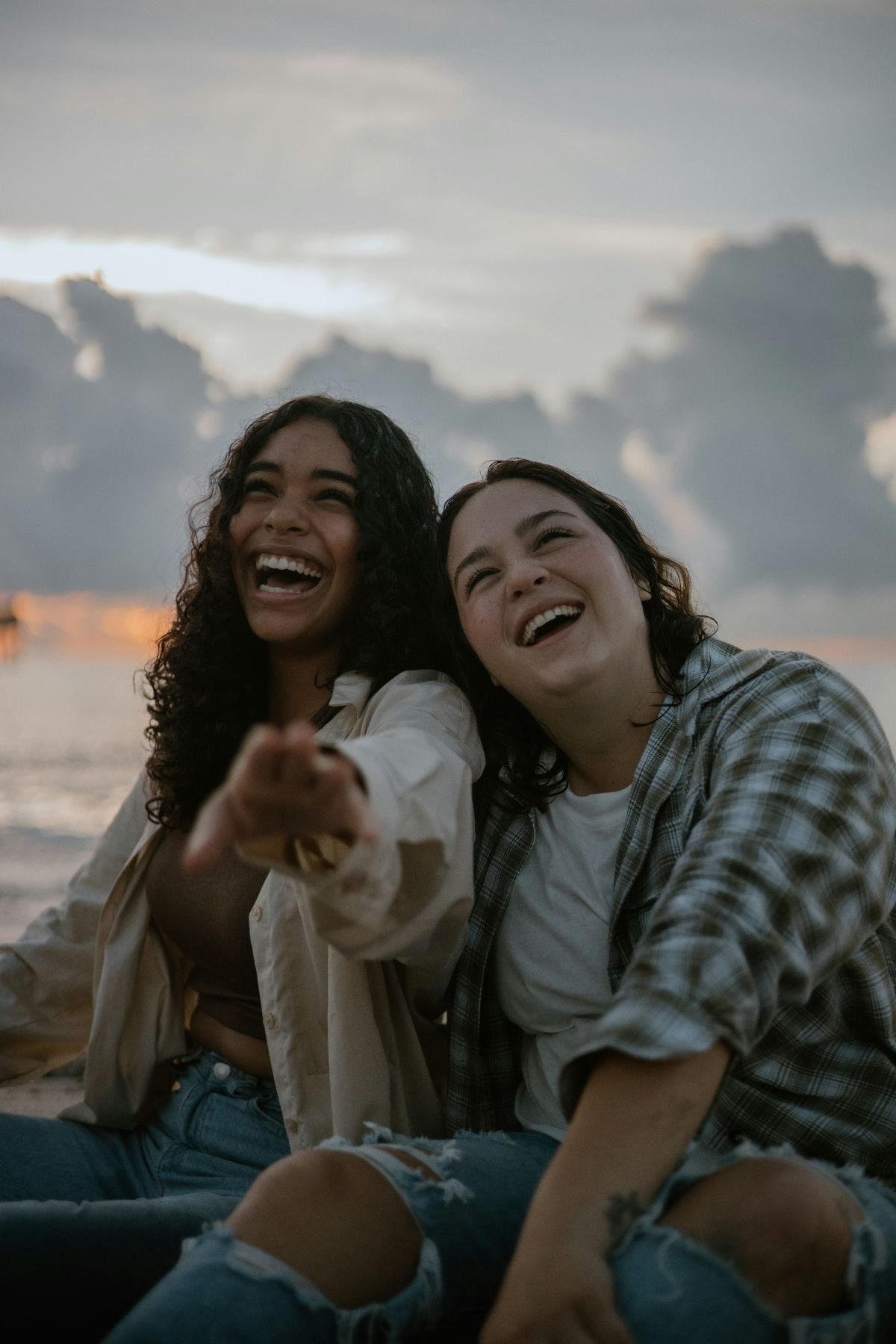 Two friends laughing together at the beach at sunset