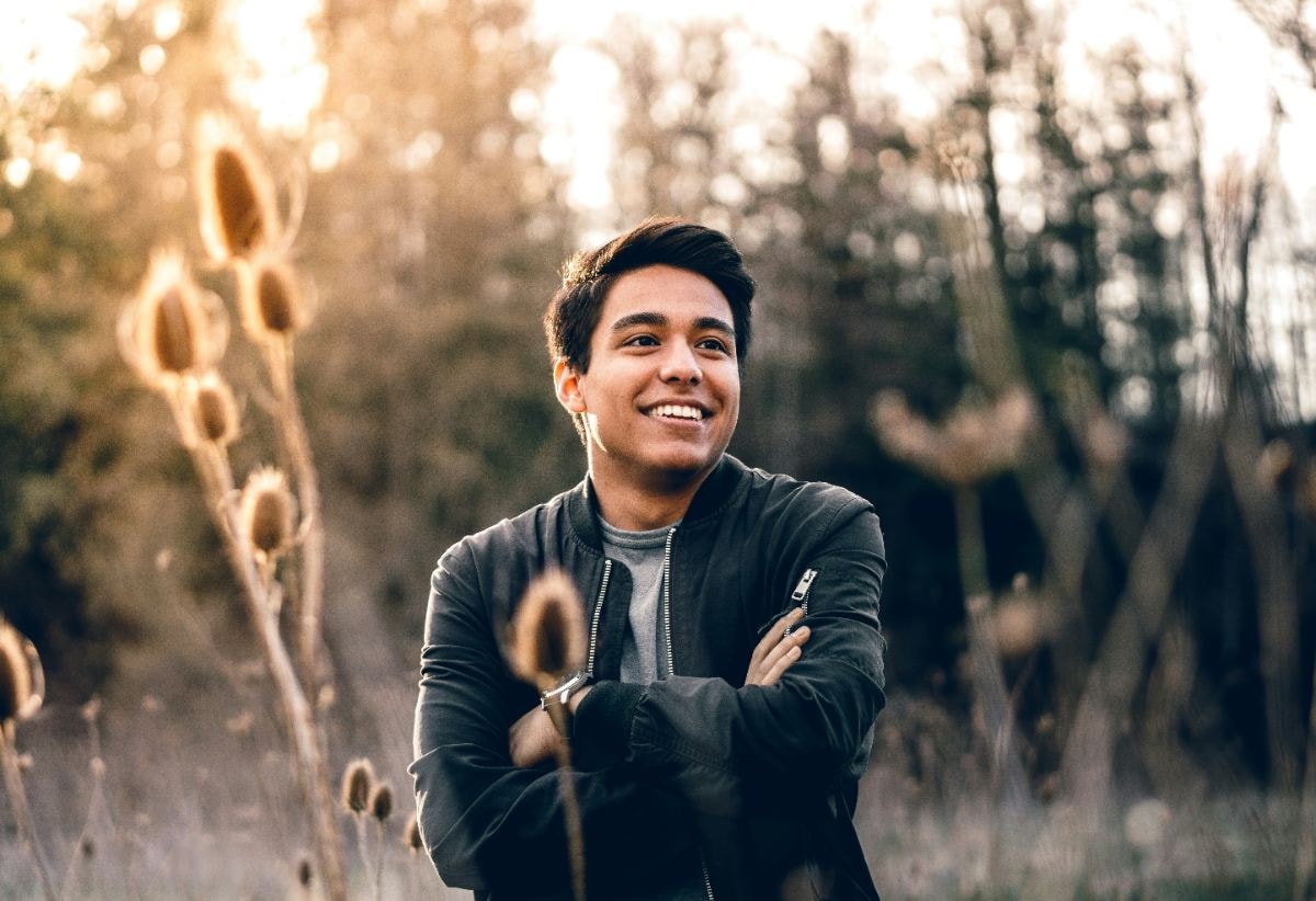 Smiling young man with arms crossed in a golden field at sunset