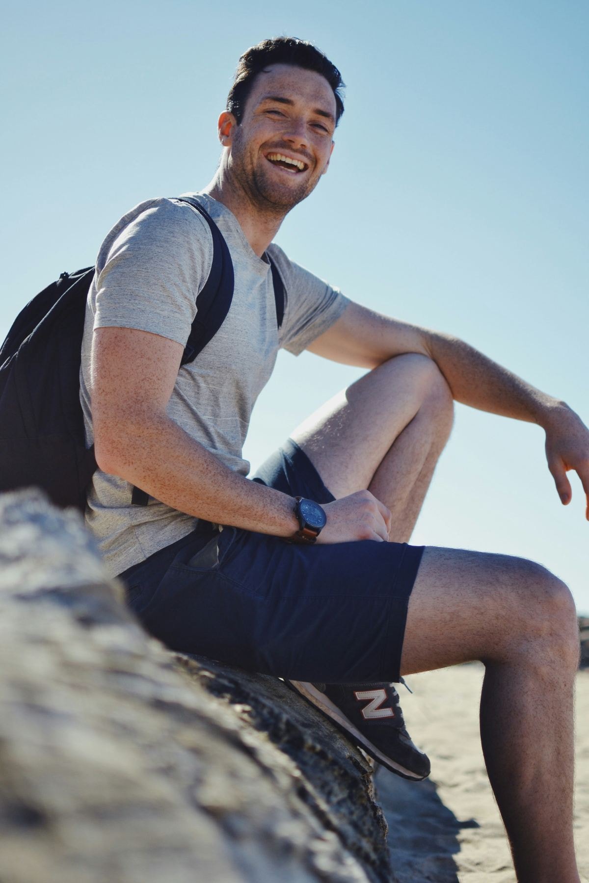 Smiling man with a backpack sitting on a rock outdoors