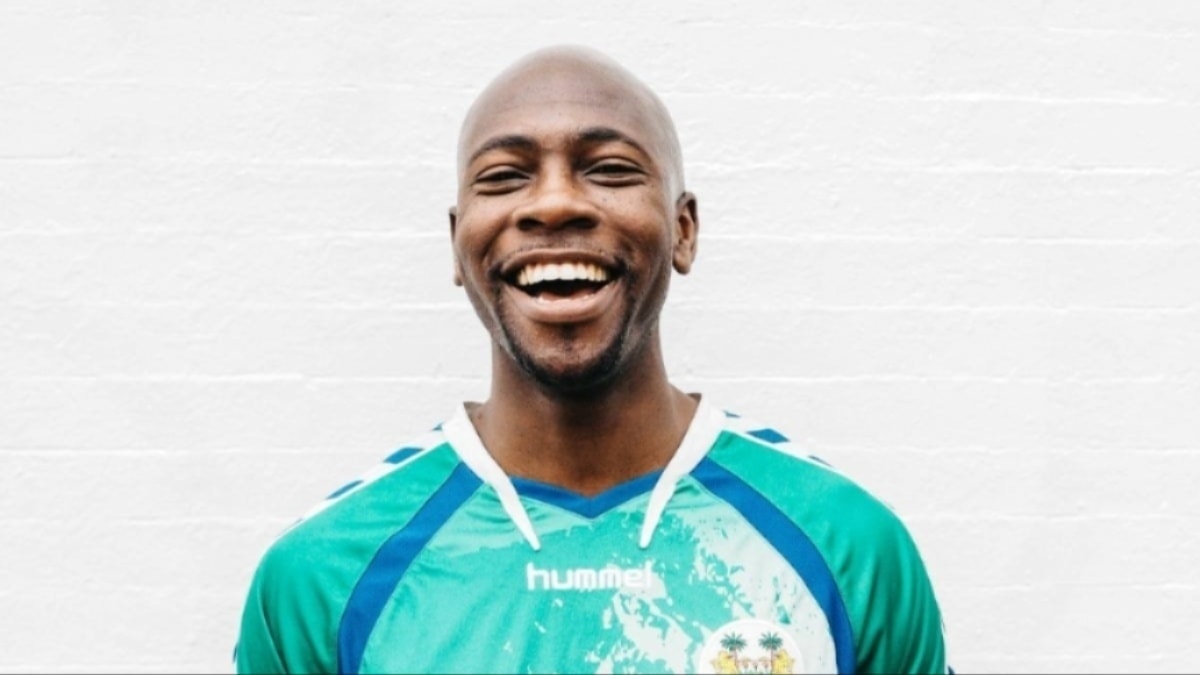 Smiling man in a teal sports jersey against a white wall